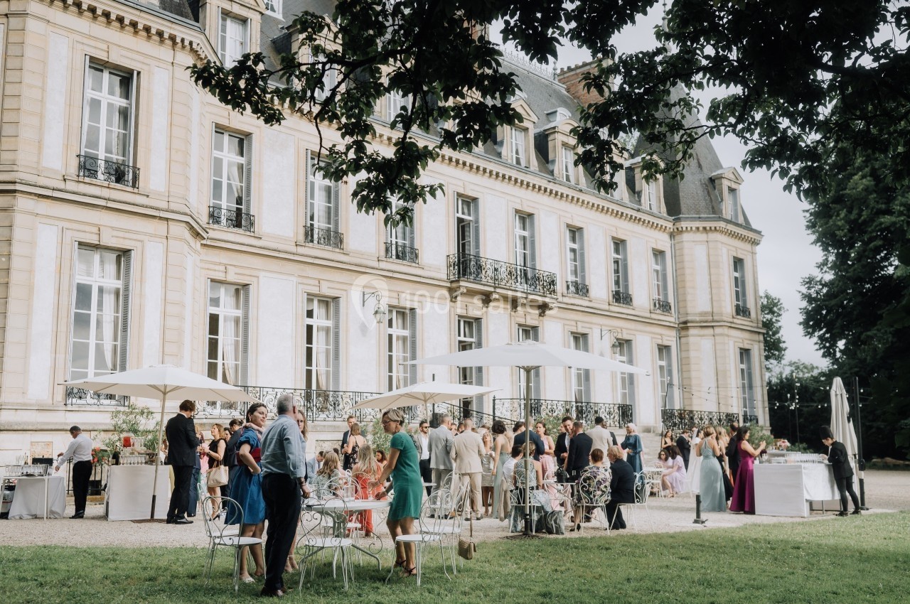 Groupe de personnes rassemblées devant un château, discutant et partageant un moment convivial en extérieur.
