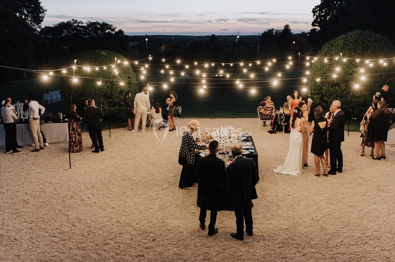Groupe de personnes rassemblées en soirée dans un jardin éclairé par des guirlandes lumineuses.
