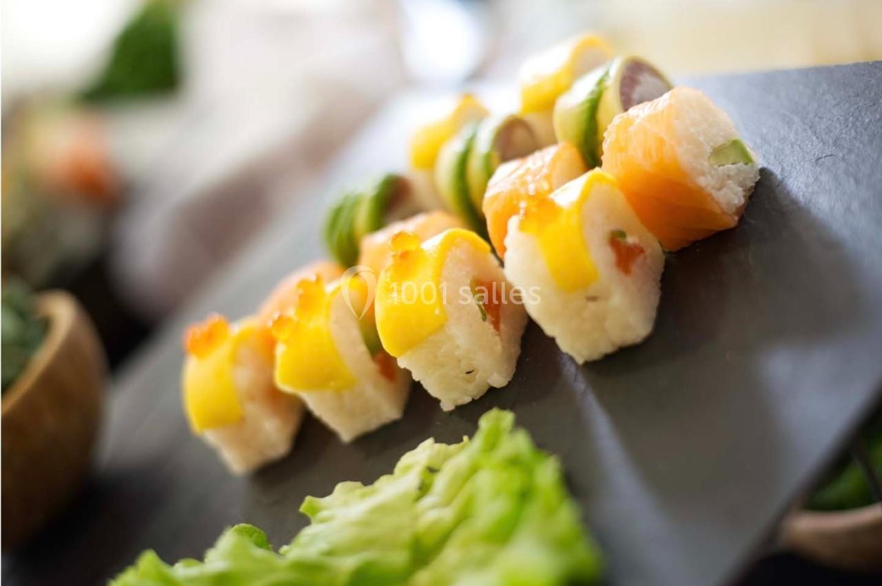 Assortiment de sushis colorés disposés sur une ardoise noire, avec une feuille de salade en premier plan.