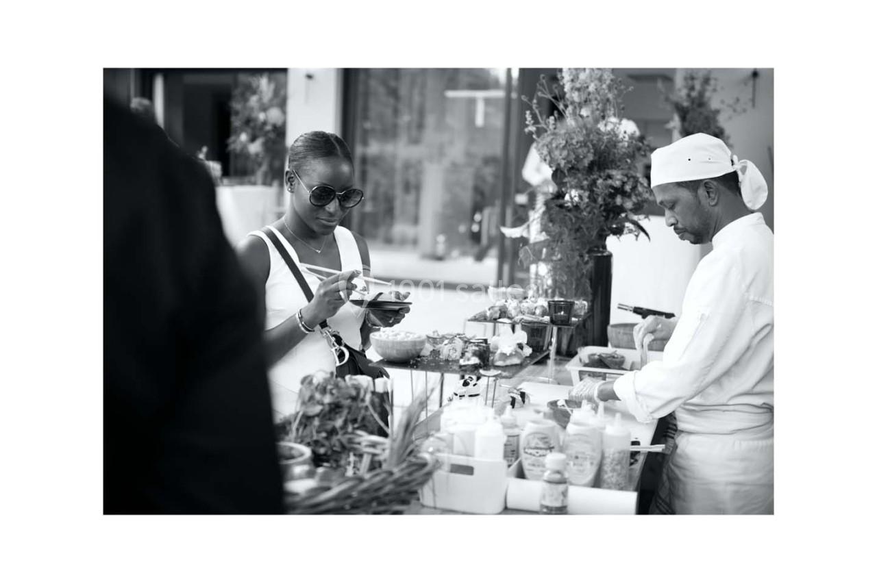 Une femme se sert de la nourriture dans un buffet en extérieur, assistée par un chef cuisinier.