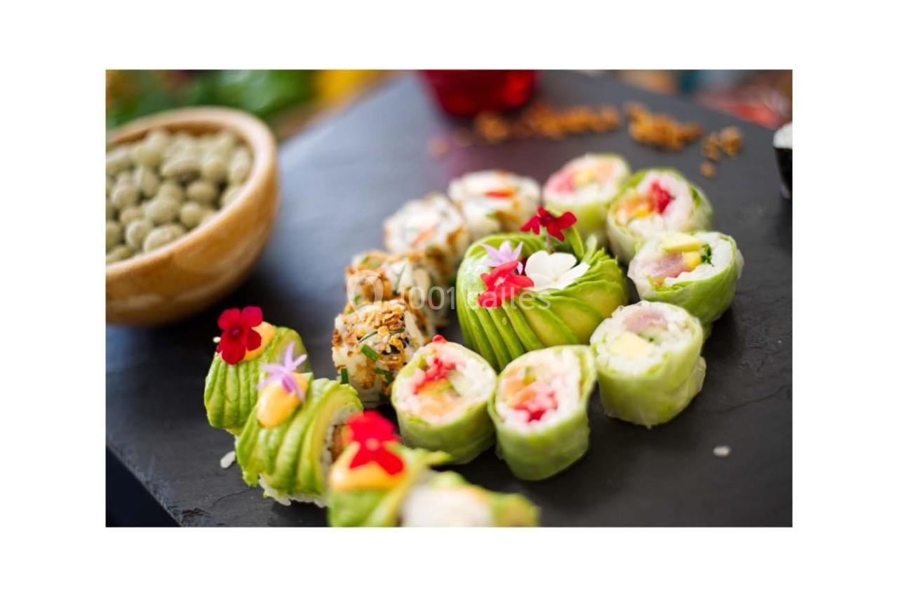 Assortiment de sushis colorés garnis de fleurs comestibles, présenté sur une ardoise noire.