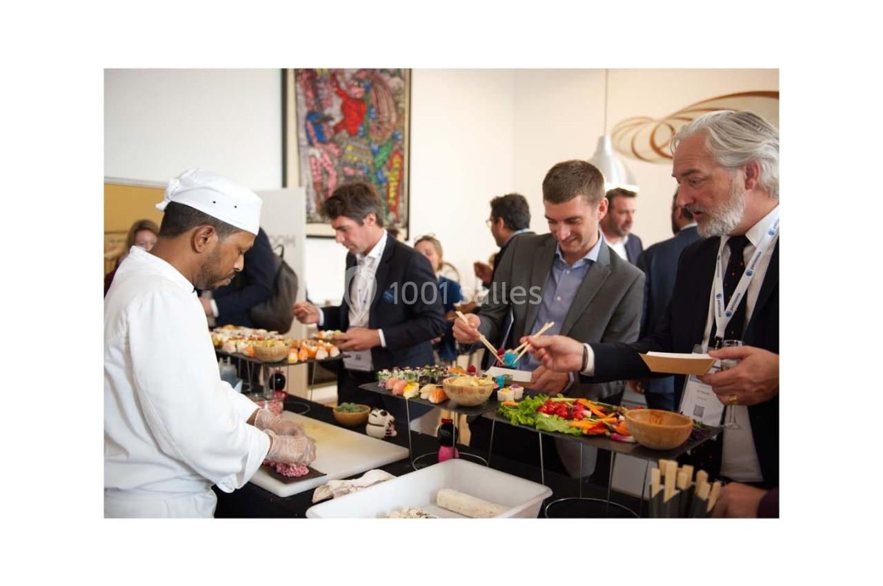 Un chef prépare des plats devant des convives en costume qui se servent à un buffet lors d'un événement.