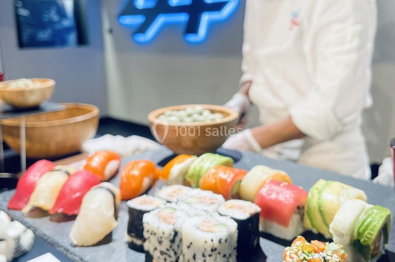 Assortiment de sushis et makis colorés présentés sur un plateau, avec un chef en arrière-plan préparant un plat.