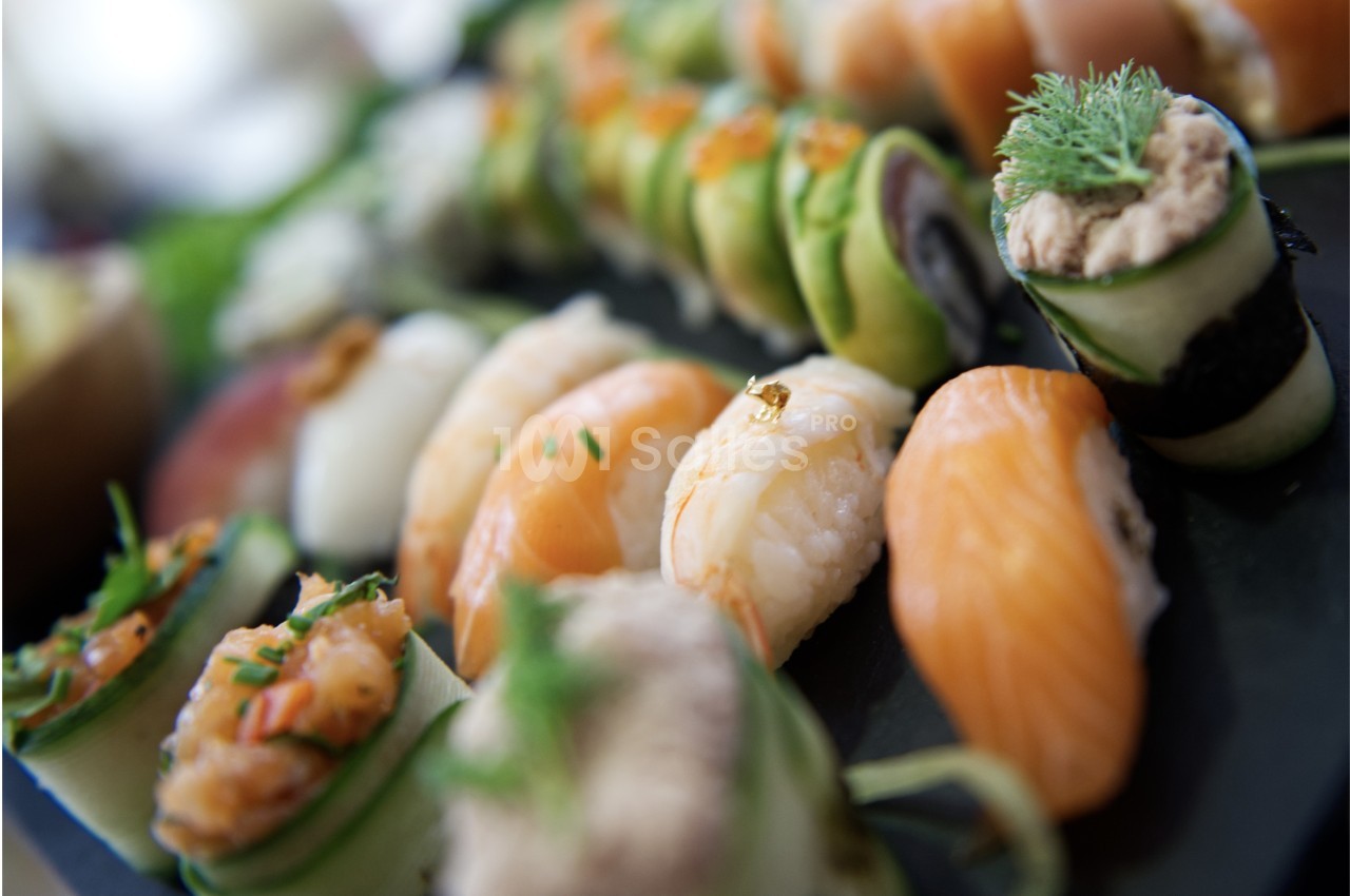 Assortiment de sushis et makis variés présentés sur un plateau noir, décorés avec des herbes et des garnitures.