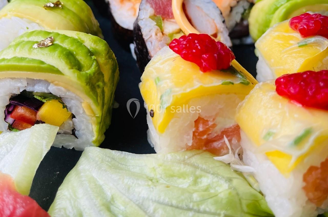 Assortiment de sushis colorés garnis de fruits, légumes, avocat et saumon, accompagnés de feuilles de salade.