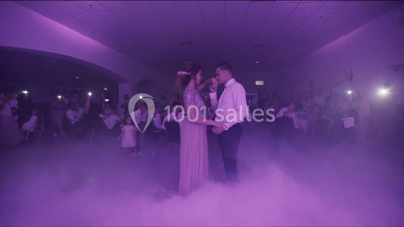 Un couple danse dans une salle éclairée de lumière violette, entouré de fumée et d'invités assis.