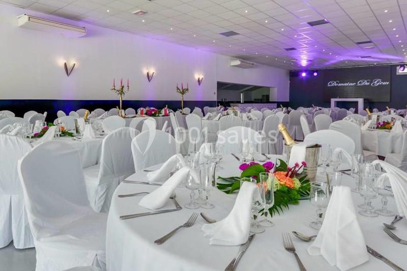 Salle de réception décorée avec des tables rondes dressées, nappes blanches et arrangements floraux colorés.