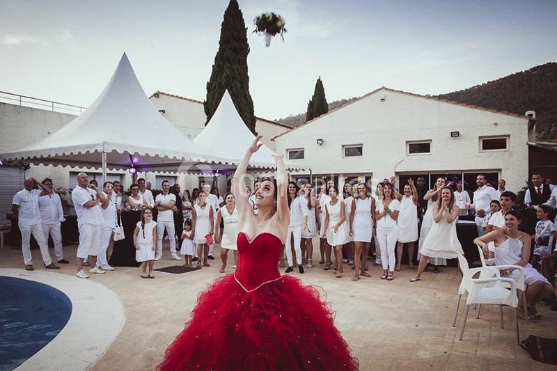Une mariée en robe rouge lance son bouquet devant des invités rassemblés près d'une piscine.