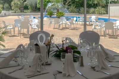 Miniature Location salle Gémenos (Bouches-du-Rhône) - Le Domaine du Gem #22 Table dressée avec nappes blanches, verres et couverts, vue sur une terrasse avec piscine et chaises en arrière-plan.
