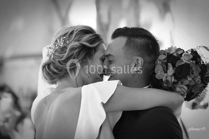Un couple s'enlace et sourit lors de leur mariage, la mariée tenant un bouquet de fleurs.