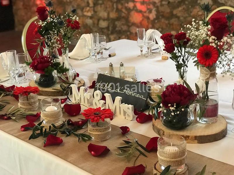 Table décorée pour un mariage avec fleurs rouges, bougies, pétales et une pancarte ’Mr & Mrs’ sur une nappe blanche.