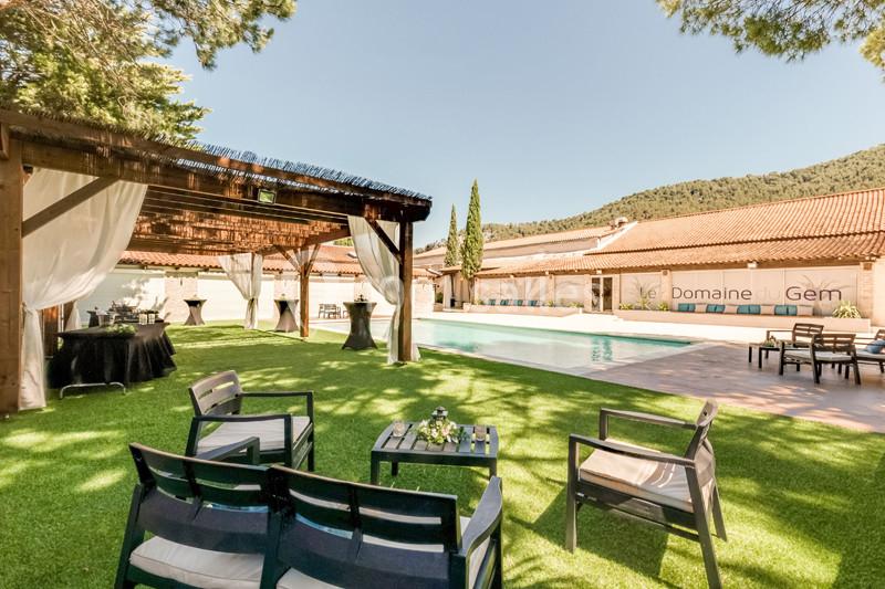 Espace extérieur avec piscine, pergolas, tables et chaises sur pelouse, entouré de collines et végétation.