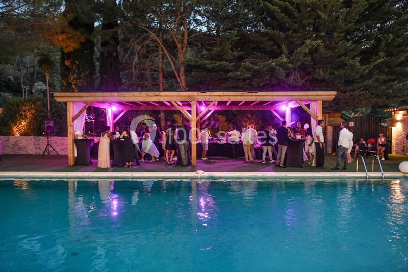 Groupe de personnes réunies sous une pergola éclairée en violet, près d'une piscine en soirée.