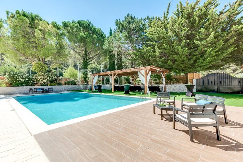 Piscine extérieure entourée de dalles en bois, pergola en bois, chaises et arbres en arrière-plan.