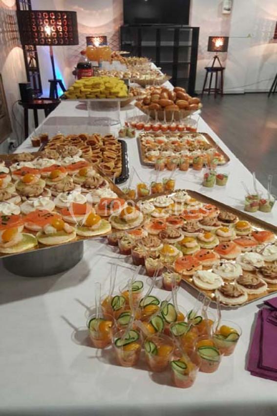 Buffet varié avec amuse-bouches, verrines, pains et desserts disposés sur une longue table blanche.