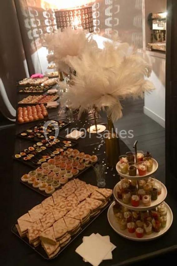 Buffet élégant avec assortiments de canapés, verrines et pâtisseries, décoré de plumes blanches dans un vase doré.