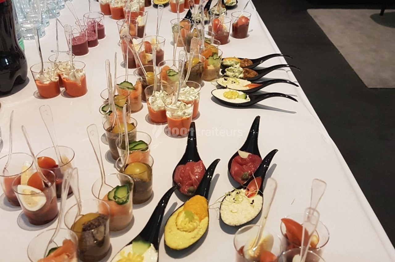 Buffet de verrines et cuillères apéritives variées disposées sur une table blanche.