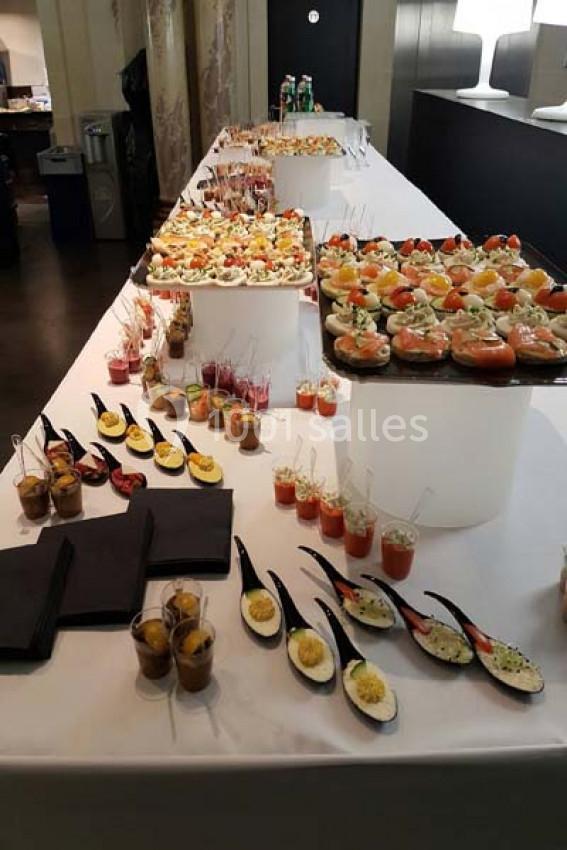 Buffet composé de verrines, cuillères apéritives et bouchées variées disposées sur une grande table blanche.