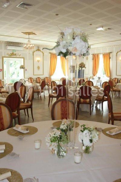 Salle de réception élégante avec tables dressées, décor floral blanc et chaises en bois rembourrées.