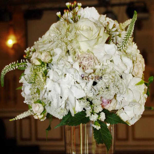 Bouquet de fleurs blanches et crème composé de roses, hortensias et autres fleurs, présenté dans un vase en verre.