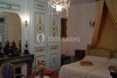 Chambre classique avec lit double, mobilier en bois, rideaux dorés et lumière naturelle entrant par une fenêtre.