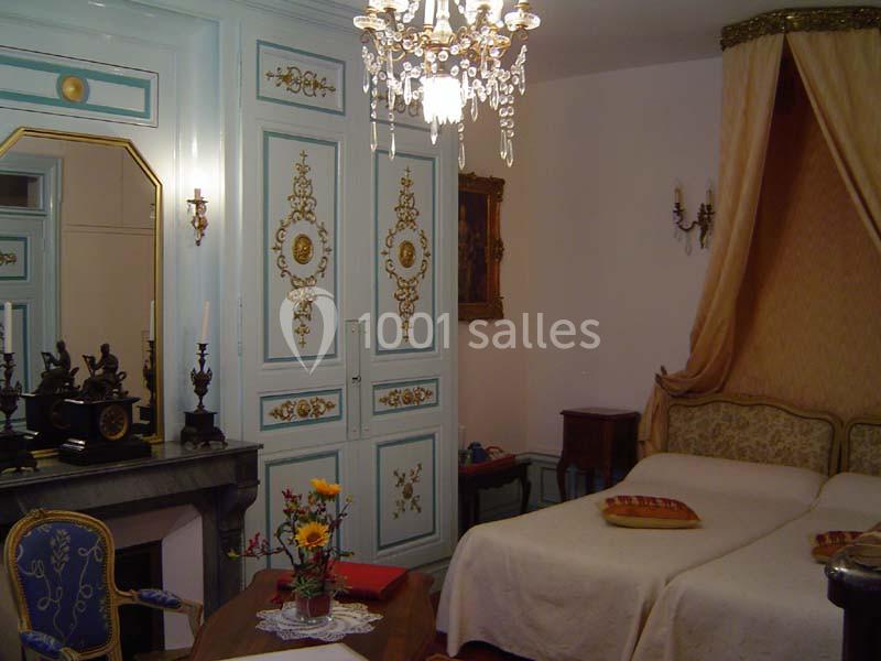 Chambre classique avec lits jumeaux, mobilier ancien, armoire ornée, cheminée et lustre dans un décor élégant.