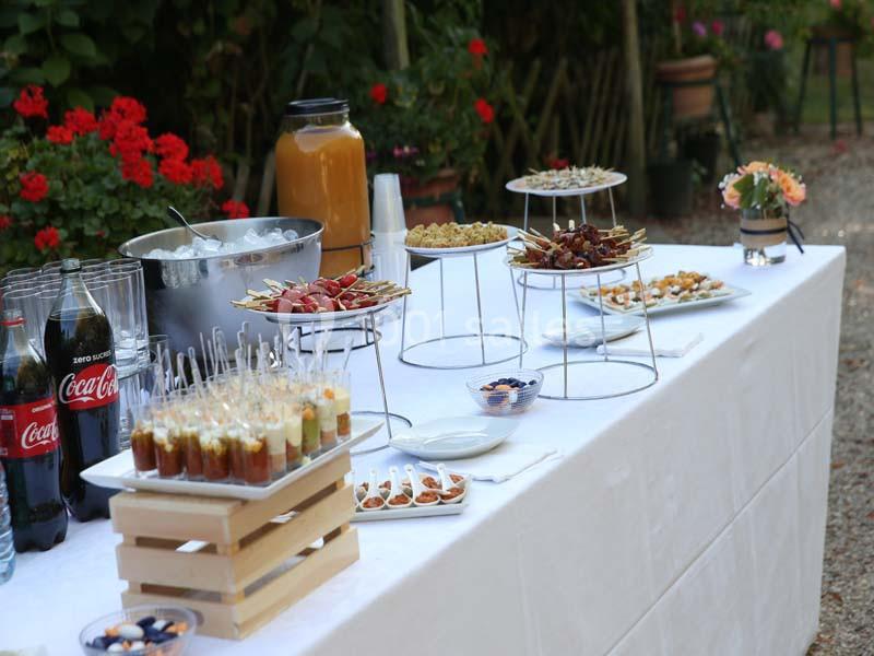 Buffet en extérieur avec boissons, verrines, brochettes et amuse-bouches disposés sur une table blanche.