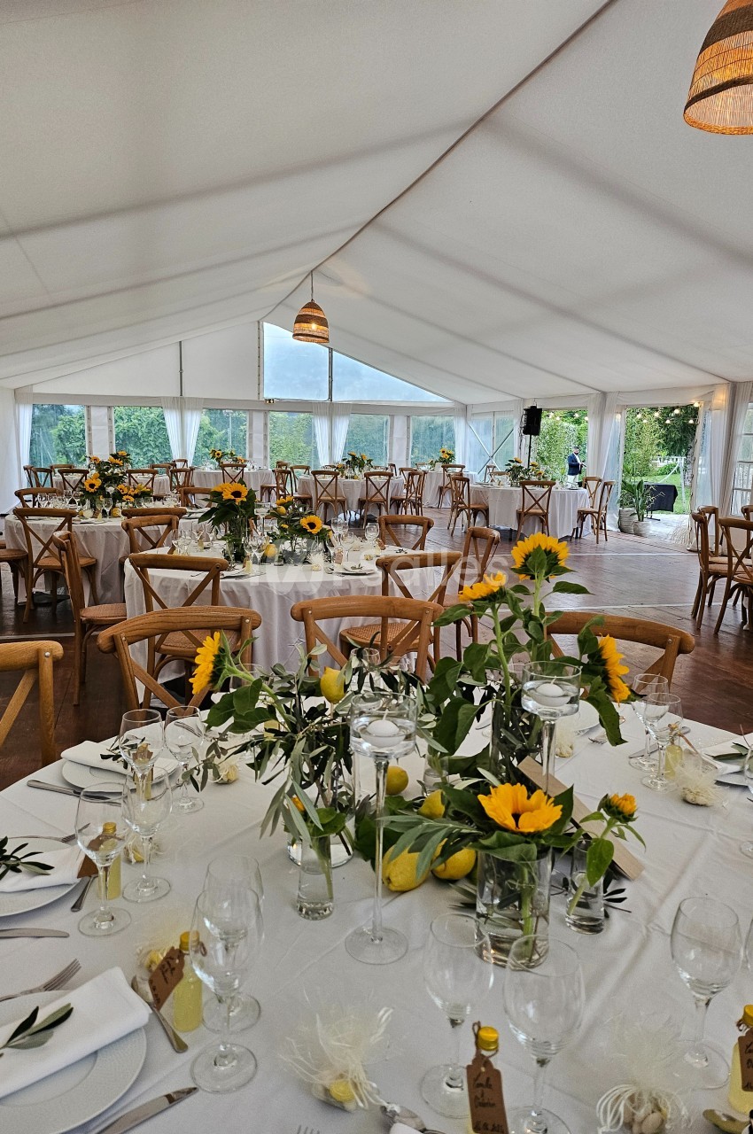 Salle de réception lumineuse sous une tente, décorée avec des tables ornées de tournesols et de citrons.