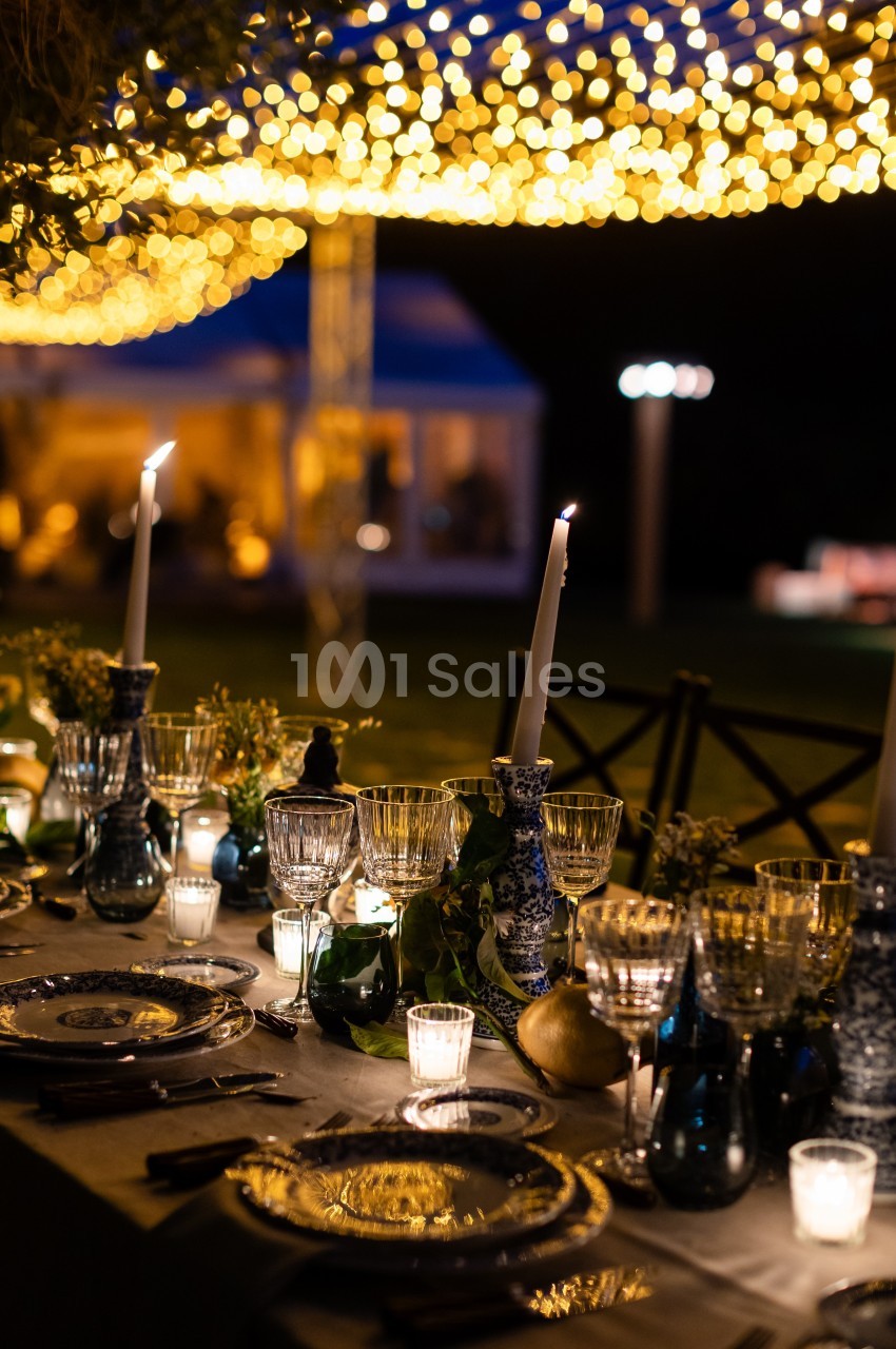 Table élégamment dressée avec chandeliers, verres et décorations sous un plafond illuminé de guirlandes lumineuses.
