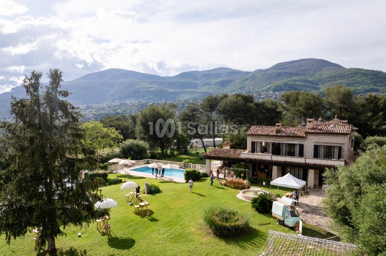 Vue d'une villa avec piscine entourée d'un grand jardin, des collines verdoyantes en arrière-plan.