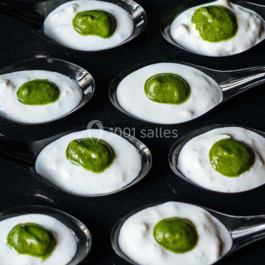 Cuillères contenant une mousse blanche garnie d'une touche de sauce verte, disposées sur une surface noire.