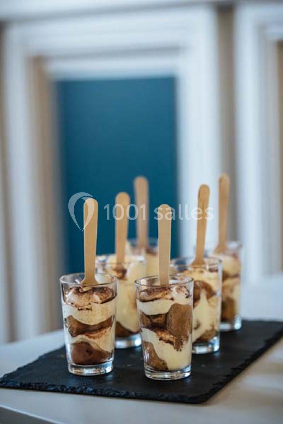 Verrines de tiramisu disposées sur une ardoise, avec des bâtonnets en bois plantés dans chaque portion.