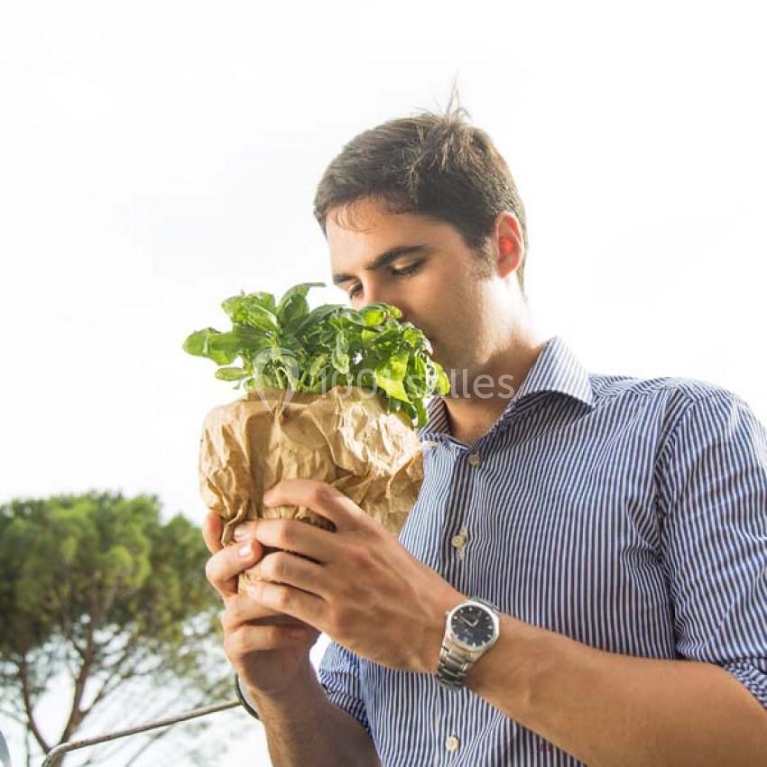 Un homme sent un bouquet de feuilles vertes enveloppé dans du papier kraft, en extérieur par temps clair.