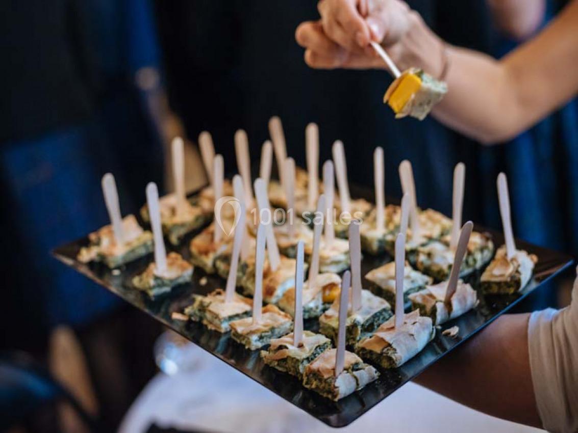 Plateau de bouchées apéritives surmontées de bâtonnets, tenu par une personne servant les invités.