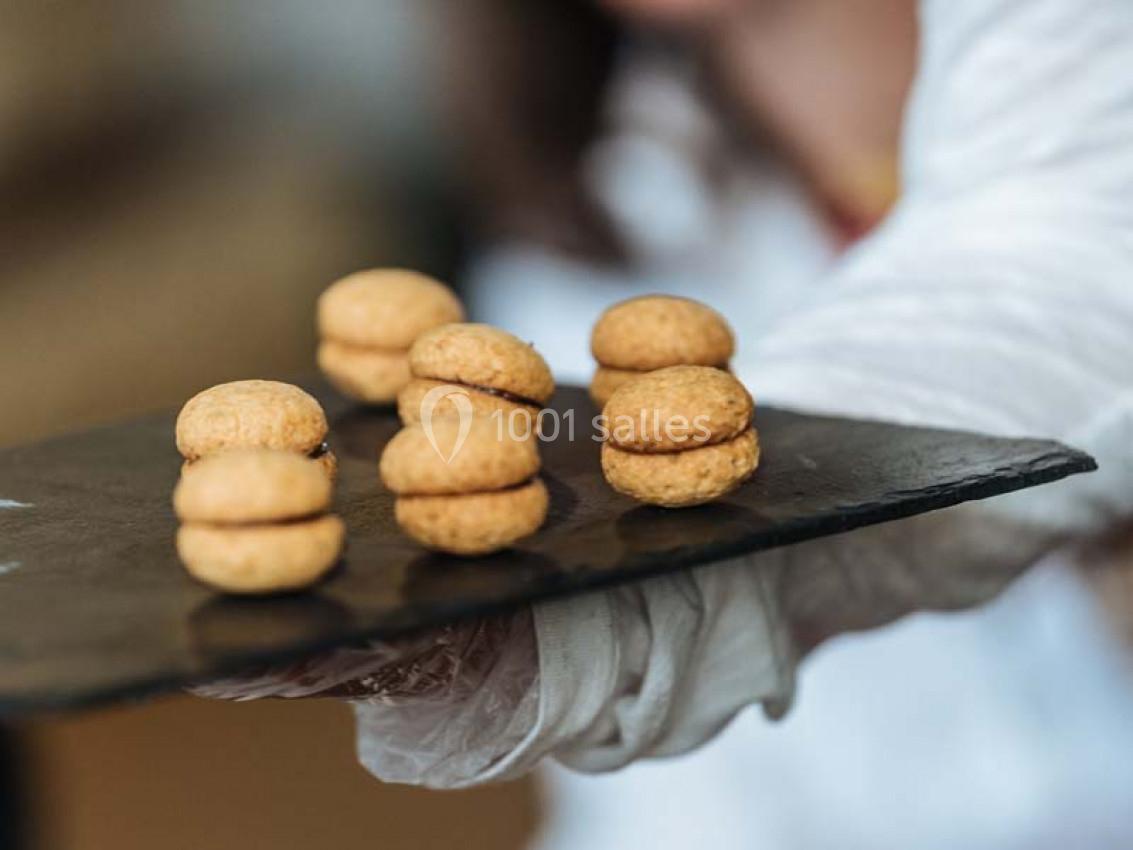 Plateau de biscuits sandwich dorés, garnis d'une crème, tenu par une personne en blouse blanche.