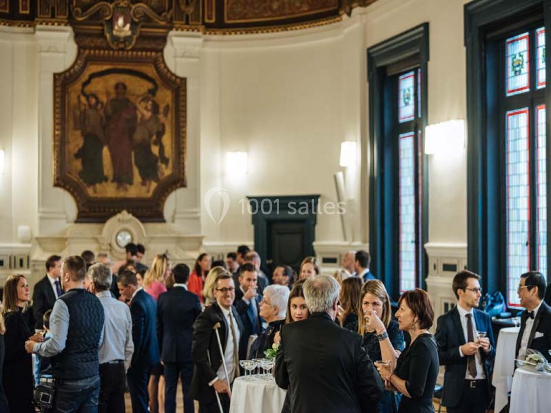 Des personnes discutent debout lors d'un événement dans une salle élégante avec des vitraux et une fresque murale.