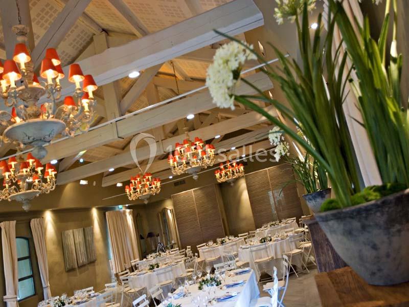 Salle de réception élégante avec tables dressées, lustres ornés de lumières rouges et plantes décoratives au premier plan.