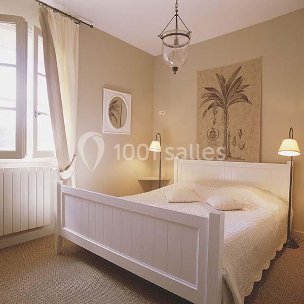 Chambre lumineuse avec un lit double en bois blanc, deux lampes de chevet et une décoration murale représentant un palmier.