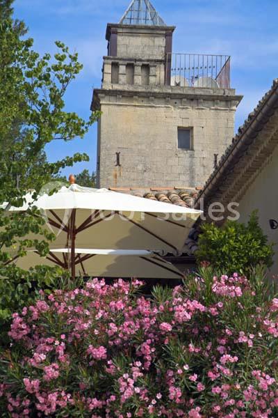 Tour en pierre ancienne entourée de végétation, avec des parasols blancs et des lauriers roses au premier plan.