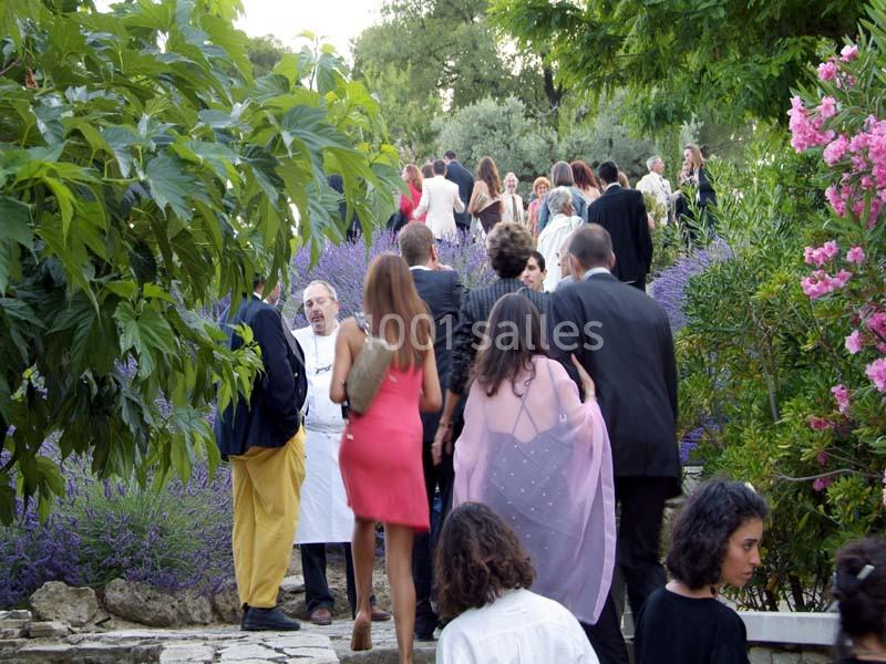 Groupe de personnes élégamment vêtues marchant dans un jardin fleuri, entouré de lavandes et d'arbres.