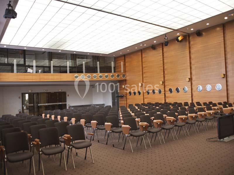Salle de conférence vide avec des rangées de chaises, un mur en bois et un plafond lumineux.