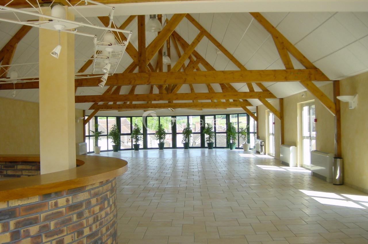 Salle lumineuse avec poutres apparentes, sol carrelé clair, grandes baies vitrées et comptoir en briques au premier plan.