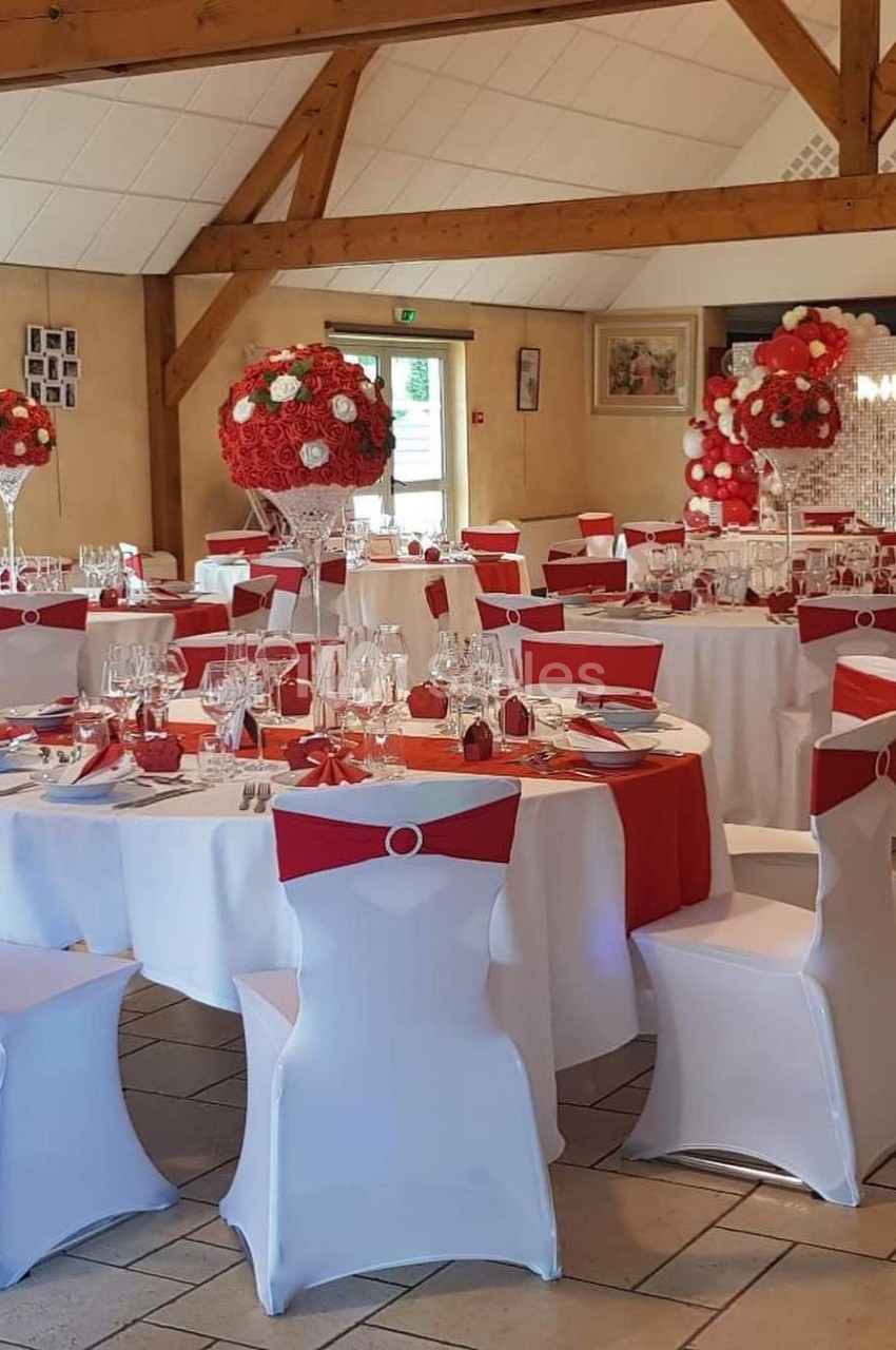 Salle de réception décorée avec des tables rondes, nappes blanches et rouges, et centres de table floraux assortis.
