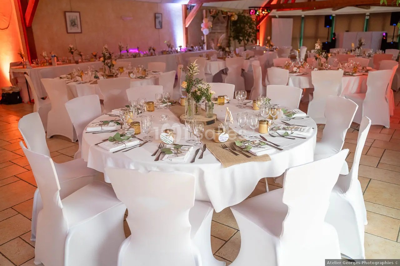 Tables rondes décorées pour un événement, avec nappes blanches, centres de table fleuris et couverts disposés.