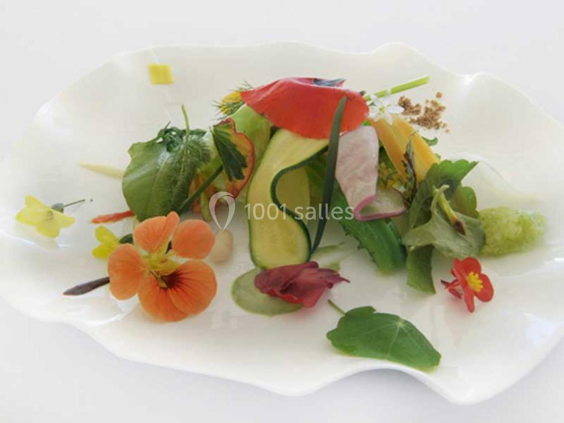 Assiette décorative composée de légumes frais, fleurs comestibles et herbes, présentée sur un fond blanc.