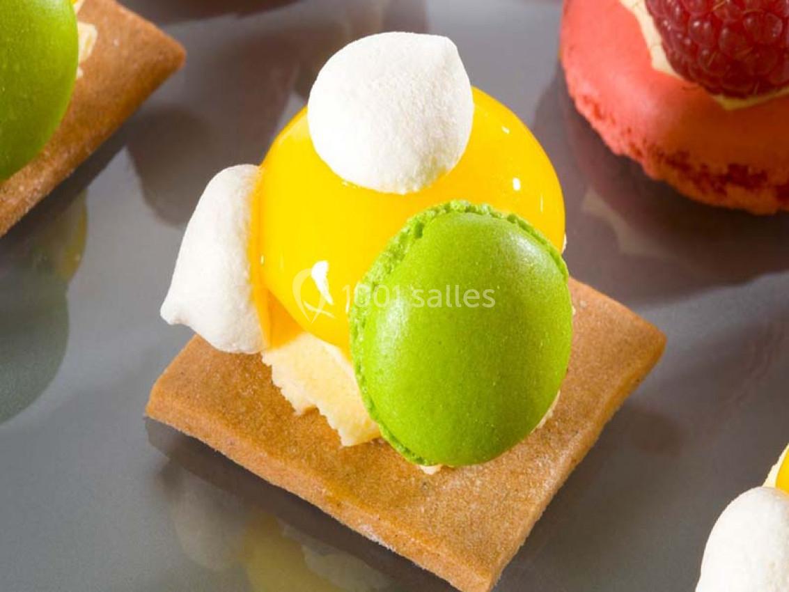 Pâtisserie composée d'un biscuit, d'une crème jaune brillante, de meringues blanches et d'un macaron vert.