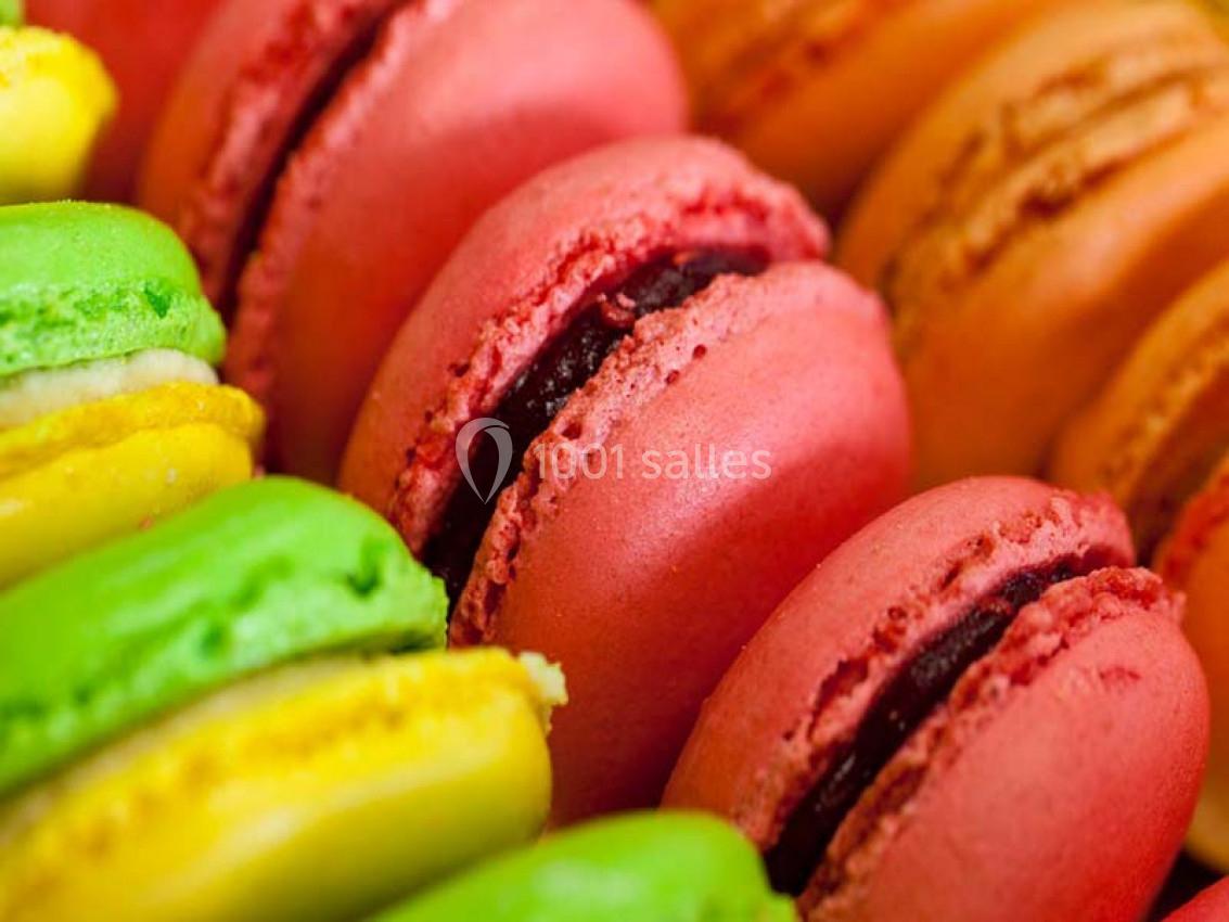Macarons colorés alignés de près, avec des coques roses, jaunes et vertes et une garniture chocolatée.