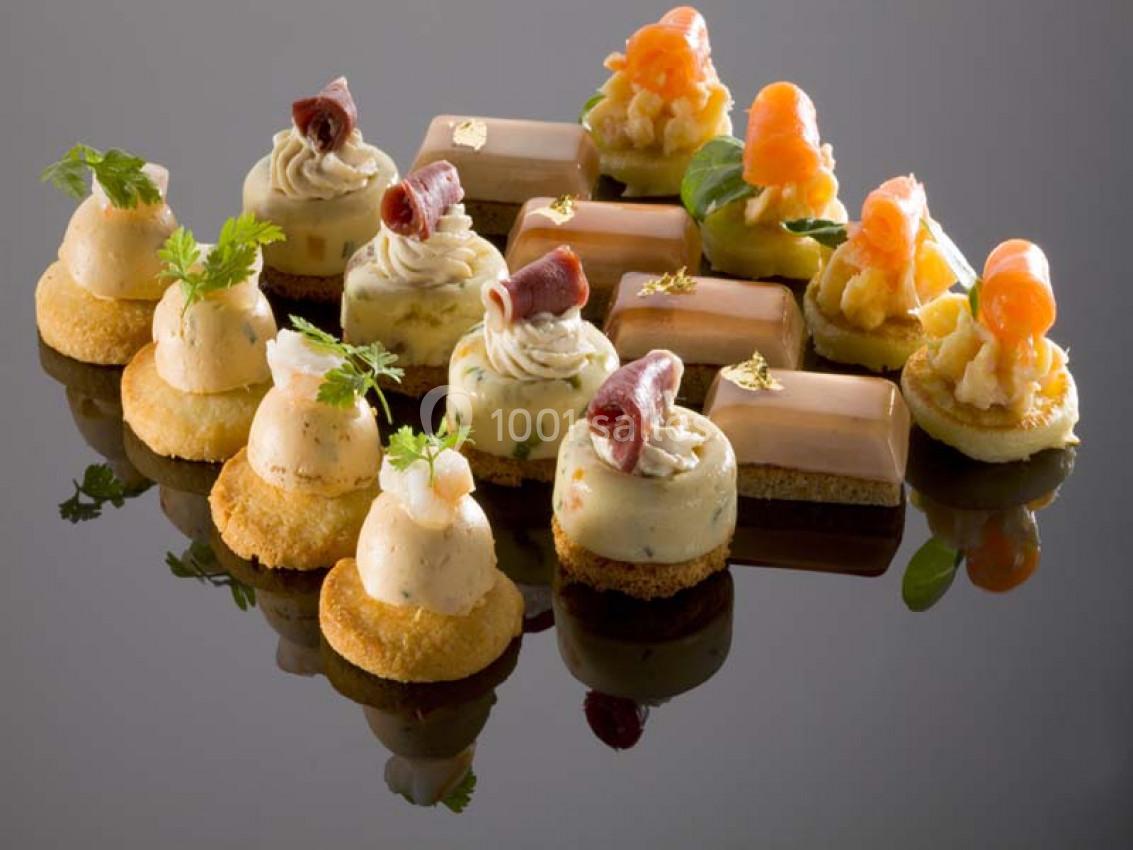 Assortiment de bouchées apéritives raffinées avec mousse, saumon fumé, jambon et décorations fines sur un plateau.