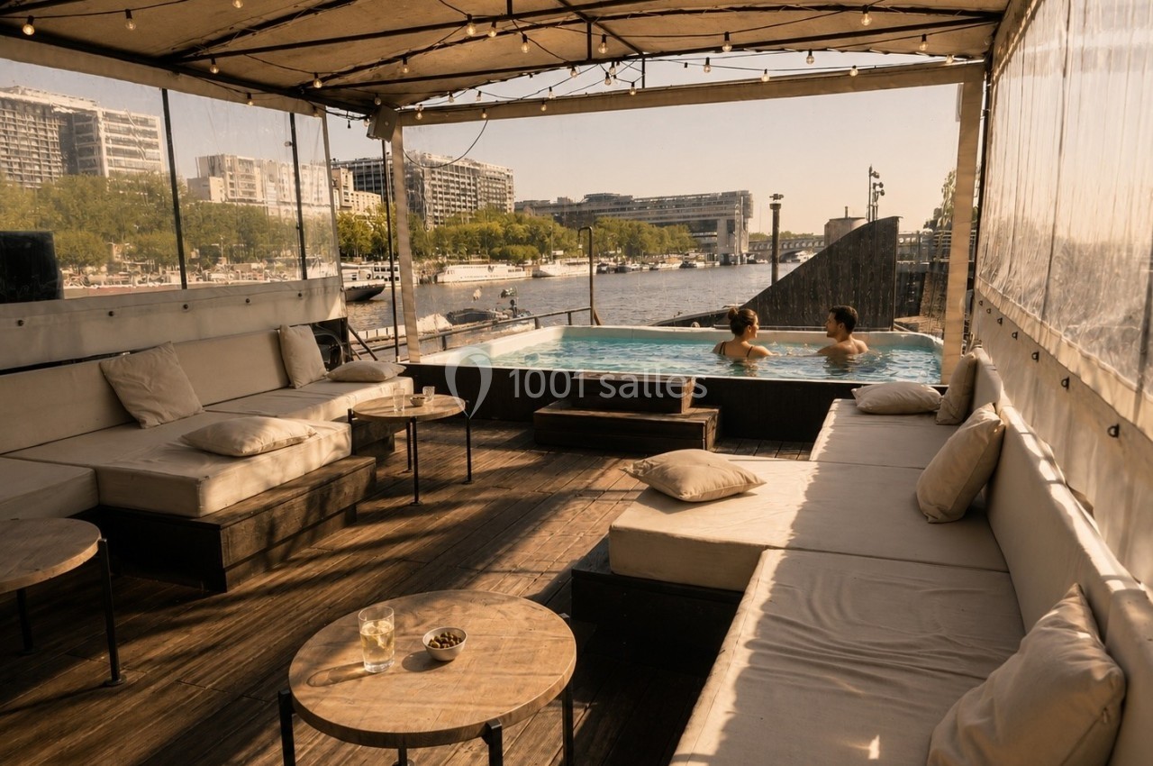 Terrasse en bois avec canapés et tables basses, vue sur une piscine et une rivière en arrière-plan.