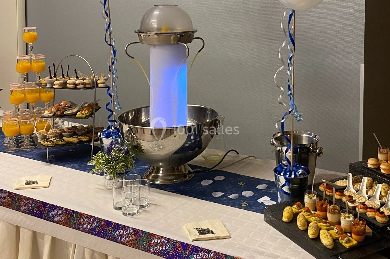 Buffet décoré avec fontaine lumineuse, verrines, amuse-bouches et boissons disposés sur une nappe blanche.